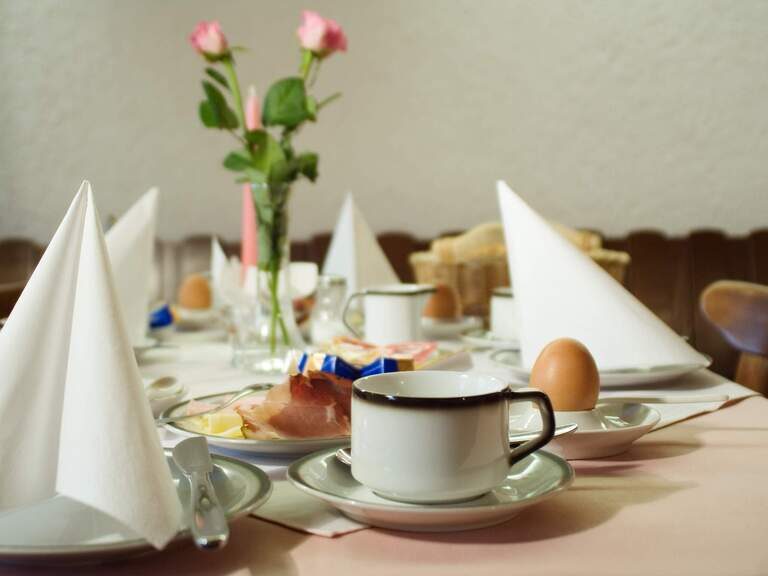 Gedeckter Frühstückstisch mit Tellern, Tassen und Servietten in einer Unterkunft von Riedl Reisen